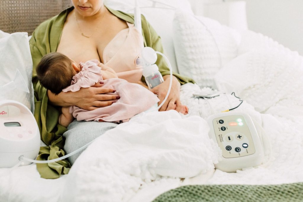 Mom breast massaging and pumping with the Nurture Breast Massager  while breastfeeding her baby
